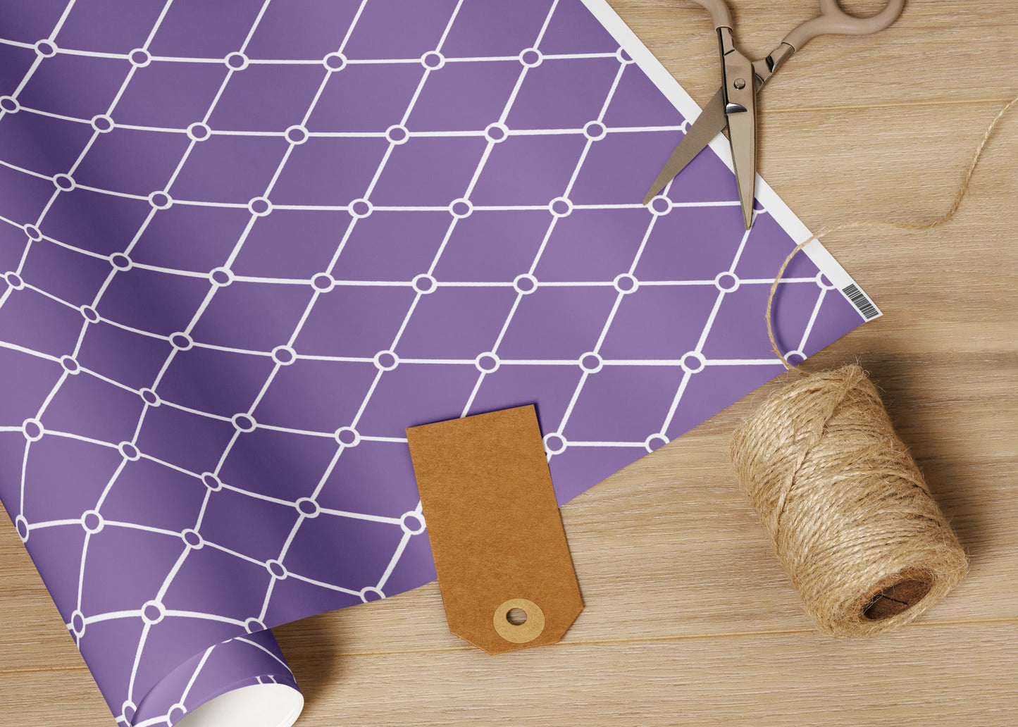 Roll of purple grid-patterned paper with scissors, twine, and leather tag on a wooden surface